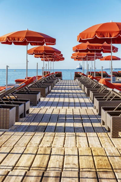 Lüks bir tatil köyünde turuncu şilteli ve şemsiyeli bir sıra iskemle. Güneşli bir gün. 