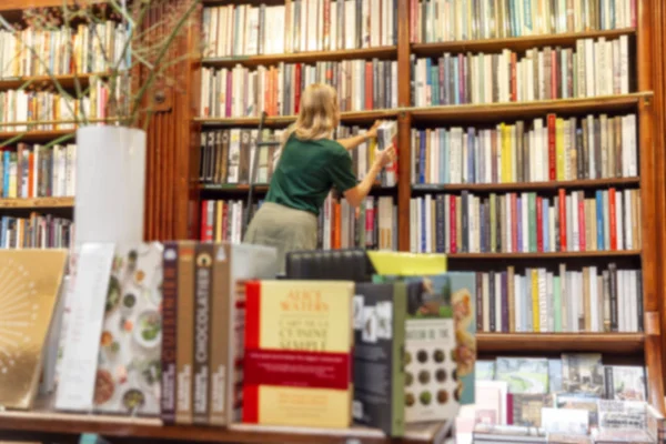 Mädchen wählt ein Buch in einer großen Buchhandlung, die auf der Treppe steht. Unschärfe. — Stockfoto