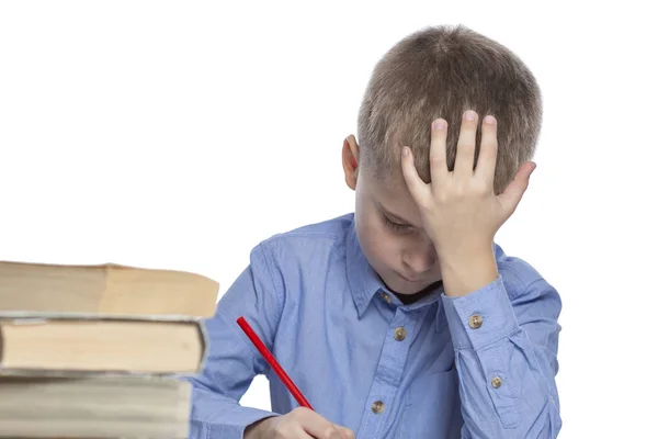 Een schooljongen doet huiswerk aan tafel. Verdriet en vermoeidheid van het studeren. Geïsoleerd over witte achtergrond. — Stockfoto