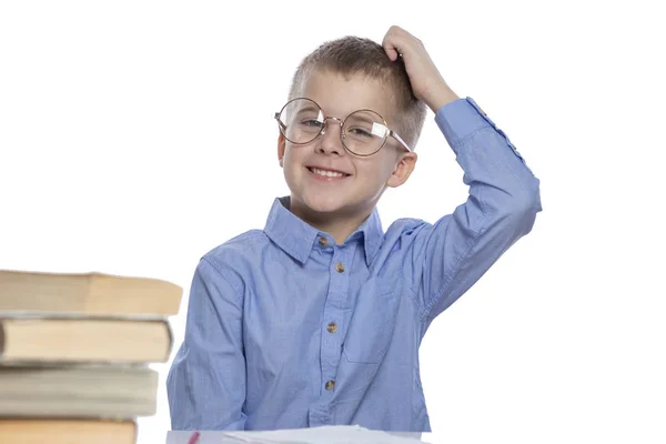 Een schooljongen met een bril zit aan een tafel en lacht. Geïsoleerd over witte achtergrond. — Stockfoto
