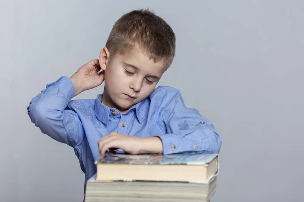 Een schooljongen doet huiswerk aan tafel. Verdriet en vermoeidheid van het studeren. Grijze achtergrond. — Stockfoto