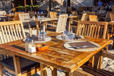 Güneşli bir günde kumlu bir sahilde, bir kafede güzel sunulan ahşap masa. Yakın plan..