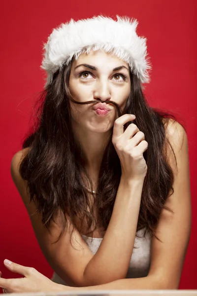 Schöne junge Frau mit Weihnachtsmann Hut lächelnd. Weihnachtsmärchen. Postkarte. roter Hintergrund. — Stockfoto