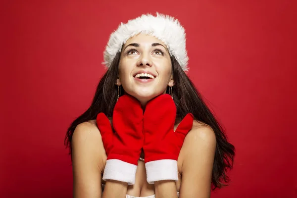 Schöne junge Frau mit Weihnachtsmann-Hut und Fäustlingen lächelnd. Weihnachtsmärchen. Postkarte. Raum für Text. roter Hintergrund. — Stockfoto