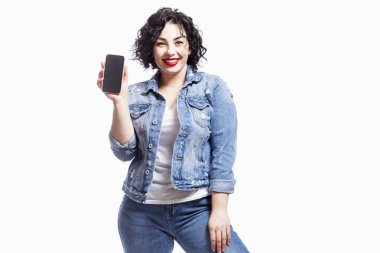 Kot pantolonla dans eden güzel bir genç kız gülüyor. Kıvırcık saçlı bir esmer, siyah ekranlı bir telefon gösteriyor. Beyaz arkaplan üzerinde izole edilmiş.