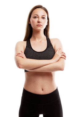 Spor giyimli, ciddi derecede narin genç bir kız kolları göğsünde çapraz duruyor. Spor ve sağlık. Beyaz bir arka planda izole edilmiş. Dikey.