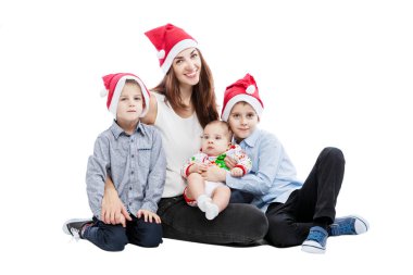 Noel Baba şapkalı üç çocuklu gülümseyen genç bir anne yerde oturuyor. Şefkat ve aile mutluluğu. Yeni yıl ve Noel kutlaması. Beyaz bir arkaplanda izole edilmiş.