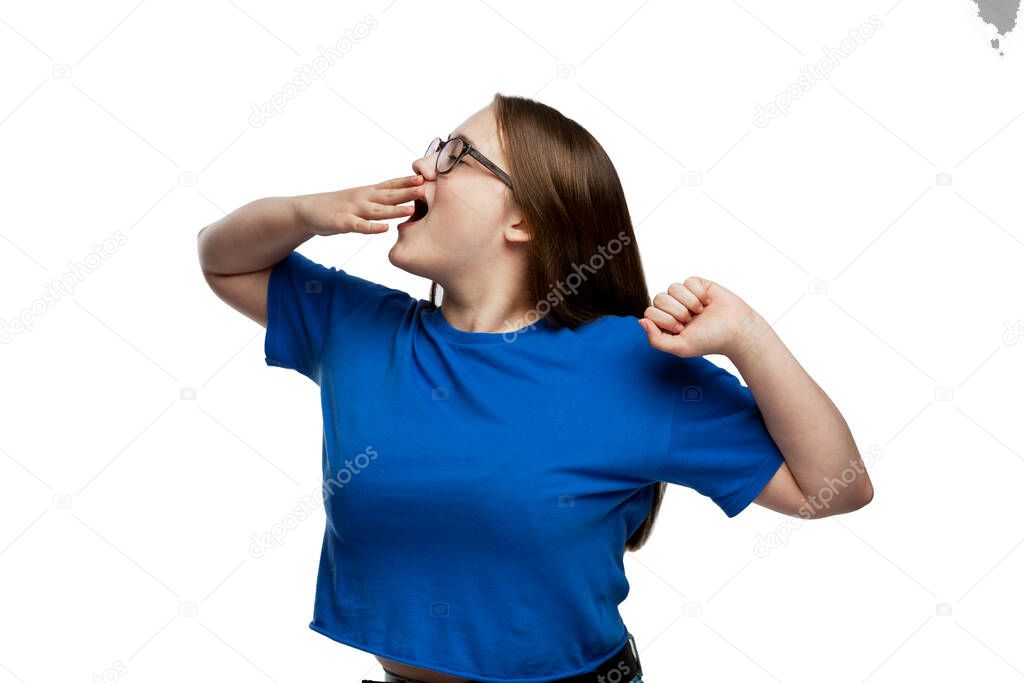 A young girl in a blue T-shirt sweetly yawns and stretches. Early morning rise and fatigue. Isolated on a white background.