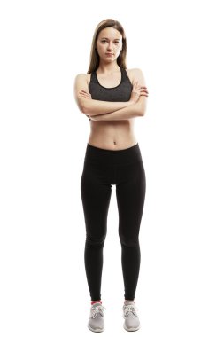 Spor giyimli ciddi bir genç kız kollarını kavuşturmuş duruyor. Spor ve aktivite. Beyaz bir arka planda izole edilmiş. Dikey.