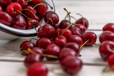 Hafif ahşap bir arka planda ve bir kasede dağılmış olgun kiraz meyveleri. Üst Manzara. Mevsimlik Vitaminler.