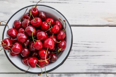 Hafif ahşap arka planda bir kasede olgun kiraz meyveleri. Mevsimlik vitaminler. Üst Manzara. Metin için boşluk.