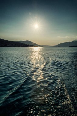 Denizde parlak güneş, dağların arka planında. Güzel, sakin bir manzara. Dikey.