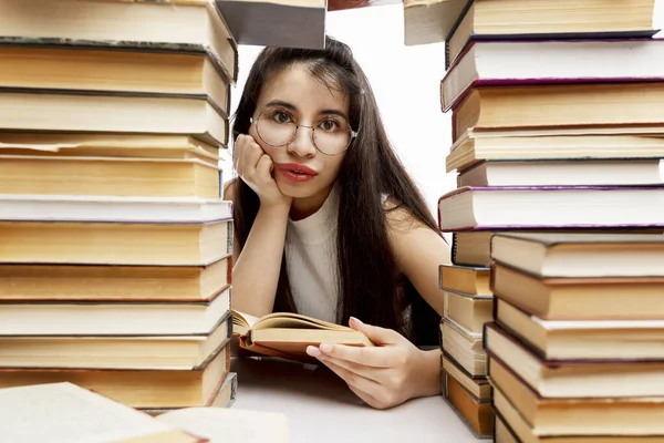 若い女の子が本の山とテーブルに座っている 眼鏡をかけた悲しいブルネット 訓練と教育 — ストック写真