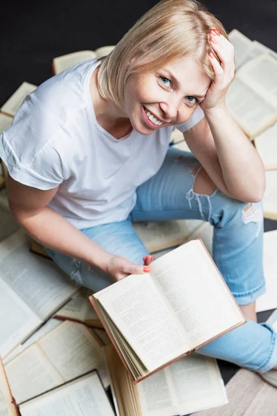 Een Glimlachende Jonge Blonde Vrouw Zit Met Een Stapel Boeken — Stockfoto