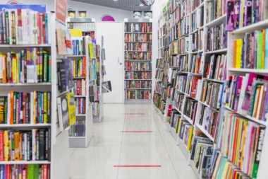 Kitaplar bir mağazada raflarda. Büyük bir edebiyat çeşidi. Bulanık. Koronavirüs salgını sırasında müşteri mesafesini korumak için yerde işaretleme.