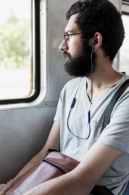 Trende kulaklıklı genç bir adam var. Sakallı bir esmer pencereden içeri bakıyor. Dikey.