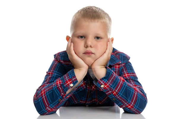 太くて悲しい少年は頭を手にテーブルに座っている 遊んだシャツを着た男子生徒 学校に戻る 白い背景に隔離されている — ストック写真