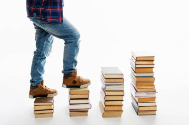 Kitap yığınlarının üzerinde kot pantolon giymiş bir çocuğun bacakları. Edebiyattan adımlar. Beyaz arka plan. Mesaj için yer var. Bilgi ve eğitim.