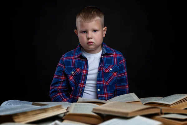 悲しい少年は本を開いてテーブルに座っている 学ぶのは難しい 黒の背景 — ストック写真