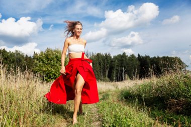 Genç bir kadın sahada koşuyor. Uzun saçlı, kırmızı etekli bir sarışın. Güneşli bir yaz gününde doğada özgürlüğün tadını çıkar. Tam yükseklik.