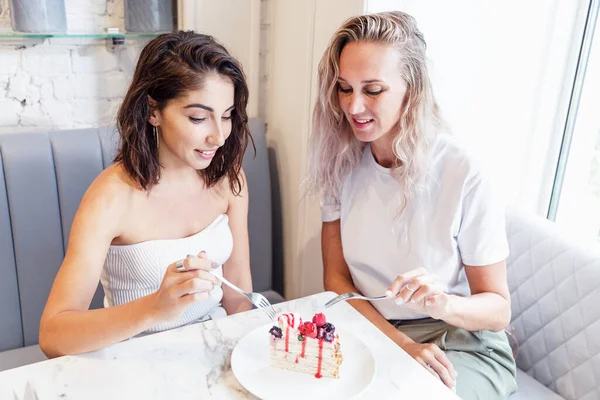 Kız arkadaşlar kafede lezzetli bir tatlı yiyorlar. Güzel gülümseyen sarışın ve esmer. Arkadaşlık ve ilişkiler.