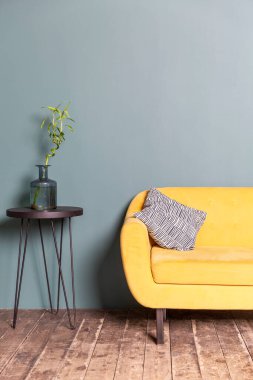Sarı kanepe ve mavi duvara karşı dekoratif çiçekli bir masa. Evin içinde şık bir iç mekan. Dikey.