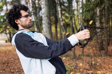 Gözlüklü genç bir adam sonbahar parkında menteşelerle meşgul. Spor ve hareket