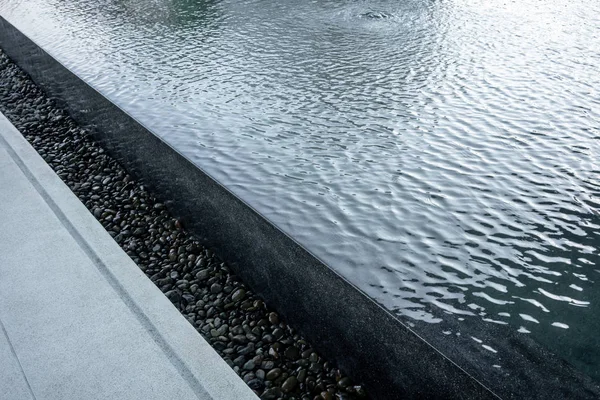 Black pool with overflow water system decorated with black gravel for public space. Landscape design detail.