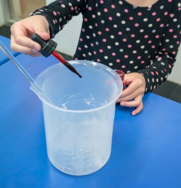 Kırmızı renk mavi masada bir plastik kabı içine eklemek için damlacık kullanan kız. DIY el jel deneyler genç bilim eğitim.
