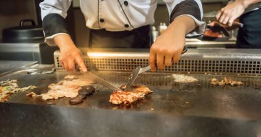 El müşterilerinin önünde sıcak tava tavuk biftek pişirme Şef. Japon Tepanyaki biftek