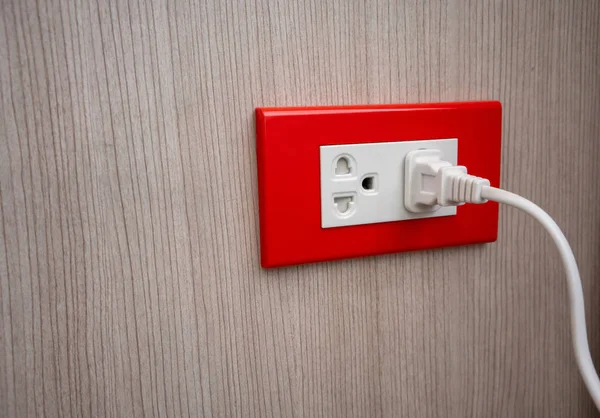 Double electrical power socket and single plug switched on wooden background.
