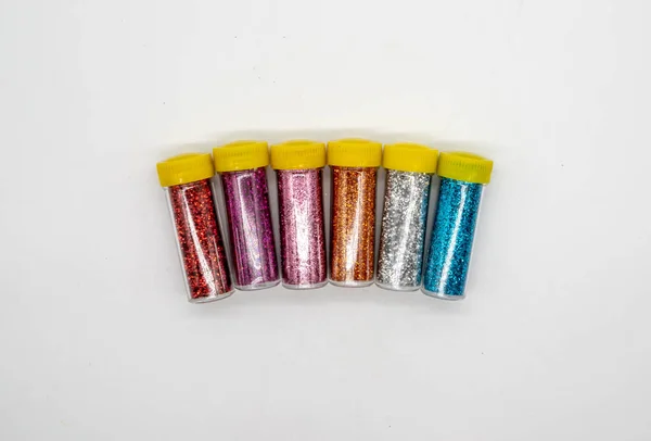 Assorted colors craft glitter in small tubes with yellow caps isolated on white background for sparkly project. Idea for DIY craft.