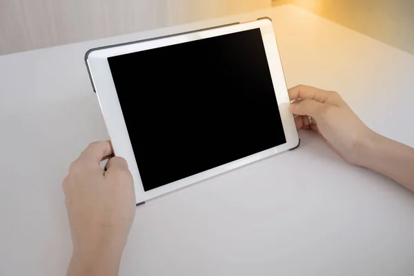 white tablet with a blank screen in the hands on white table