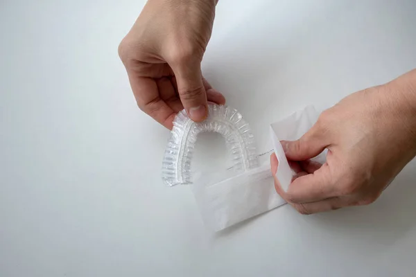 Hand opening a white package of disposable shower cap against white background in hotel bathroom.