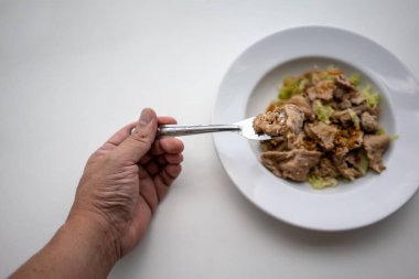 Portre bir kaşık gevrek sarımsak, biber ve beyaz arka plan üzerinde beyaz seramik tabak sebze ile kızarmış domuz eti üzerinde.