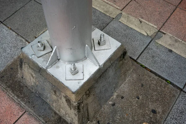 Metal pole with screw on concrete foundation in public space area. Construction detail.