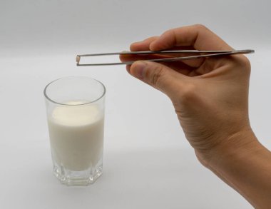 Bir bardak süt beyaz arka plan üzerinde izole üzerinde süt dişleri ve küçük kök cımbız ile tutarak teslim.