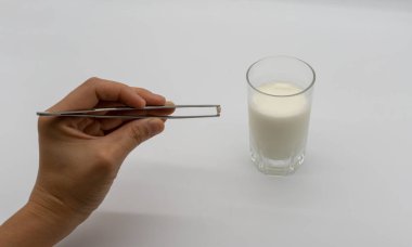 Bir bardak süt beyaz arka plan üzerinde izole üzerinde süt dişleri ve küçük kök cımbız ile tutarak teslim.