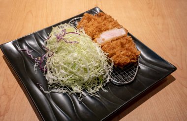 Kızarmış domuz eti tongkatsu ahşap masa üzerinde siyah seramik tabak sebze ile.