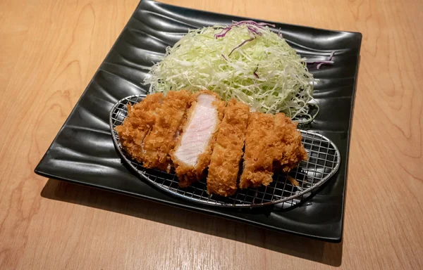 Kızarmış domuz eti tongkatsu ahşap masa üzerinde siyah seramik tabak sebze ile.