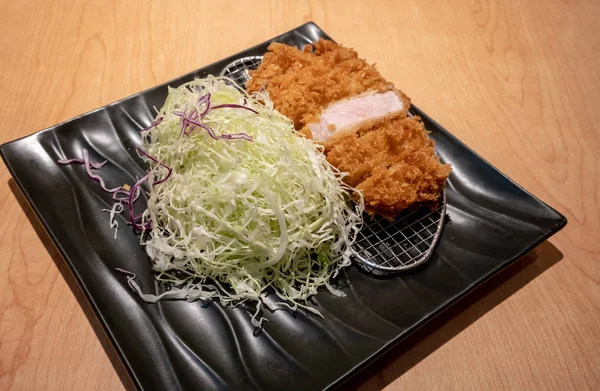 Kızarmış domuz eti tongkatsu ahşap masa üzerinde siyah seramik tabak sebze ile.