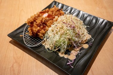 Kızarmış domuz eti tongkatsu ahşap masa üzerinde siyah seramik tabak sebze ile.