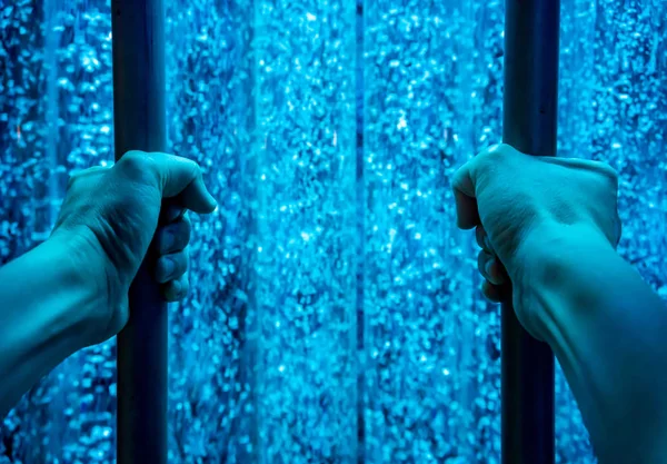 Hands holding metal bar against blue moving water background. Imprison concept.