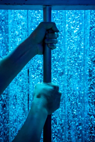Hands holding metal bar against blue moving water background. Imprison concept.