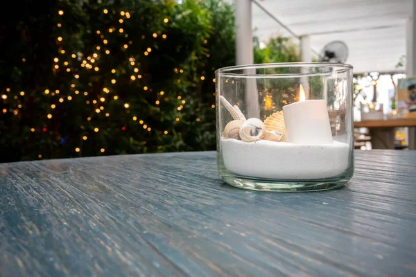 Decorative art, imitated sea in small glass. Decorative sea with sand, seashells and LED electric candle on wooden table.