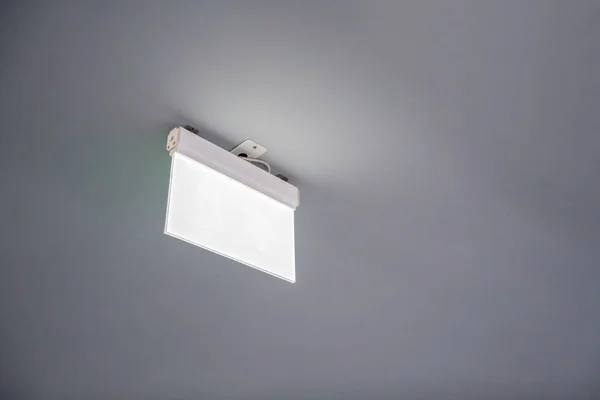 White blank rectangle sign with lighting hanging on white ceiling in building