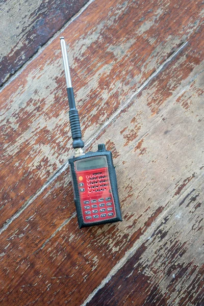 Radio transceiver. Red rectangle portable device with yellow and black buttons and silver antenna on wooden background.