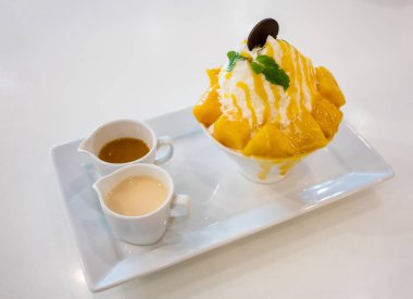 Mango Bingsu, beyaz tabak içinde servis cubed tatlı mango Topingler ile buz tatlı traş.
