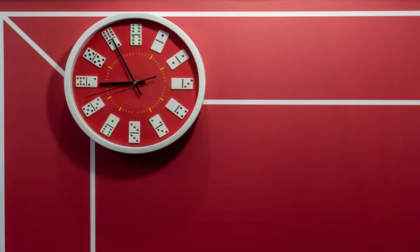 Red circle wall clock decorated with domino pieces hanging against red wall background.