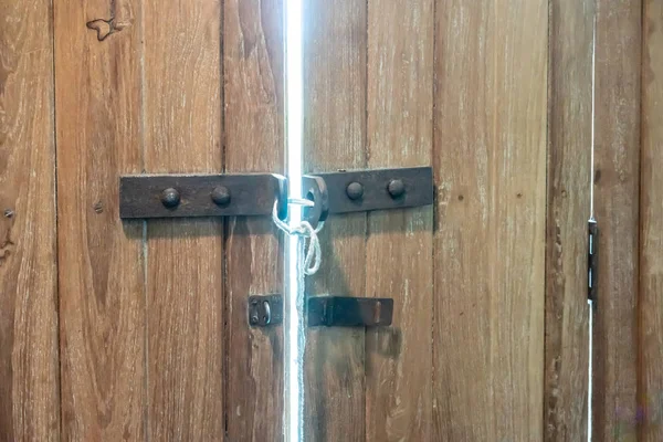 Güvenliği için beyaz iple hafif kahverengi ahşap kapı paslı mandal kilitli.